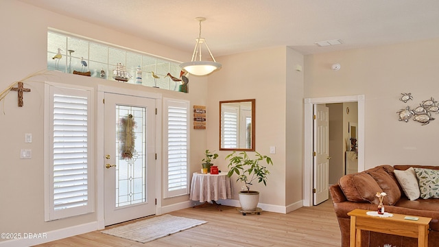 foyer entrance featuring light wood-style floors, baseboards, and a towering ceiling