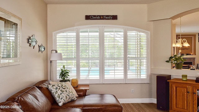 sitting room with wood finished floors, a chandelier, healthy amount of natural light, and arched walkways