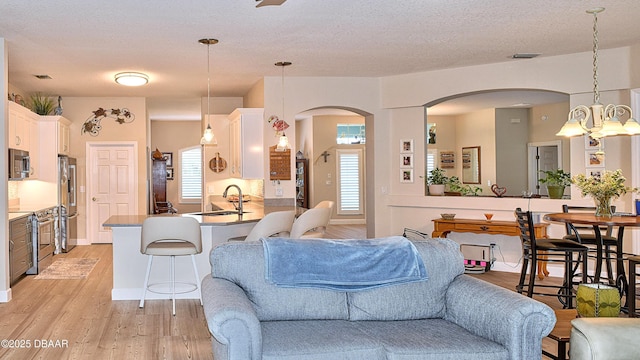 living area featuring light wood finished floors, arched walkways, a textured ceiling, and a chandelier