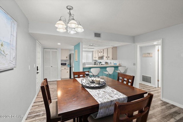 dining area with light wood finished floors, an inviting chandelier, visible vents, and baseboards