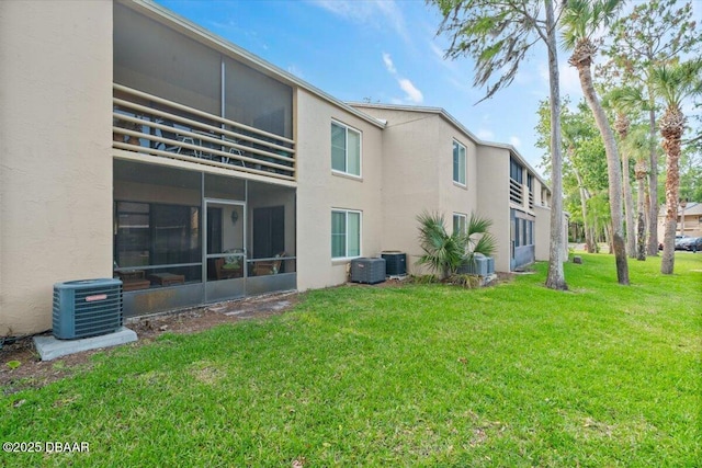 rear view of house with a lawn, central air condition unit, stucco siding, and a sunroom