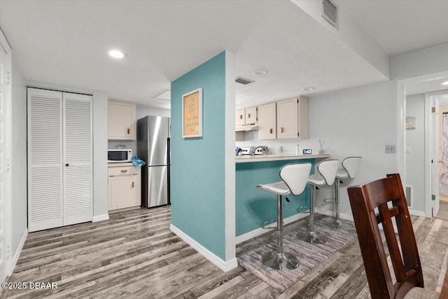 kitchen featuring baseboards, white microwave, light wood finished floors, and freestanding refrigerator