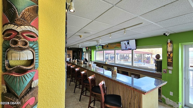 bar with a paneled ceiling, light tile patterned floors, and rail lighting