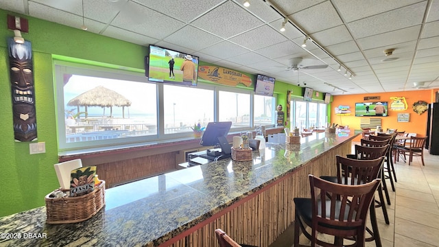 bar featuring stone counters, track lighting, tile patterned floors, and ceiling fan