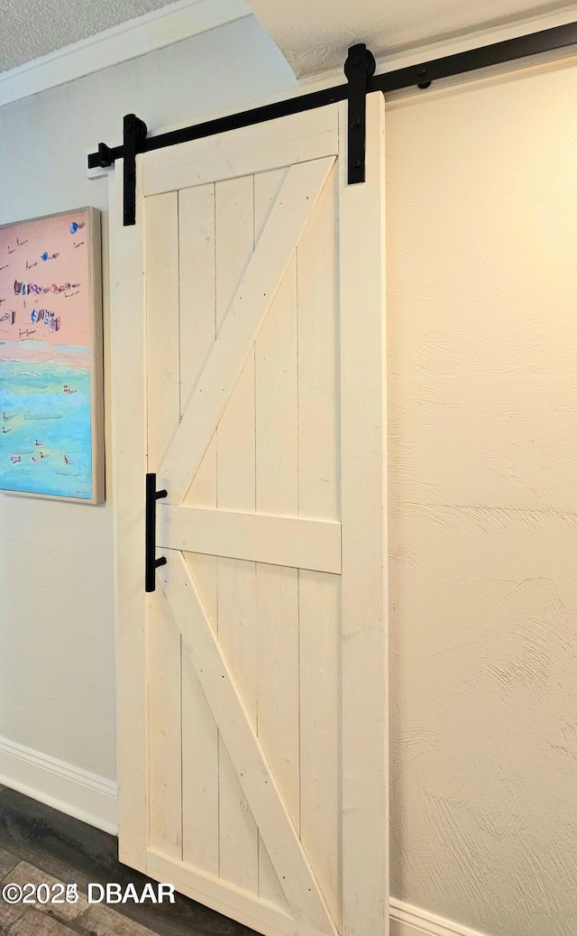 interior details with a barn door, a textured ceiling, and ornamental molding