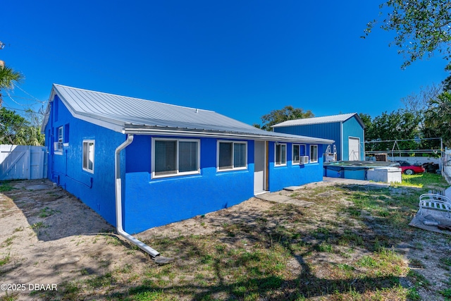 exterior space featuring an outbuilding, fence, stucco siding, a hot tub, and metal roof