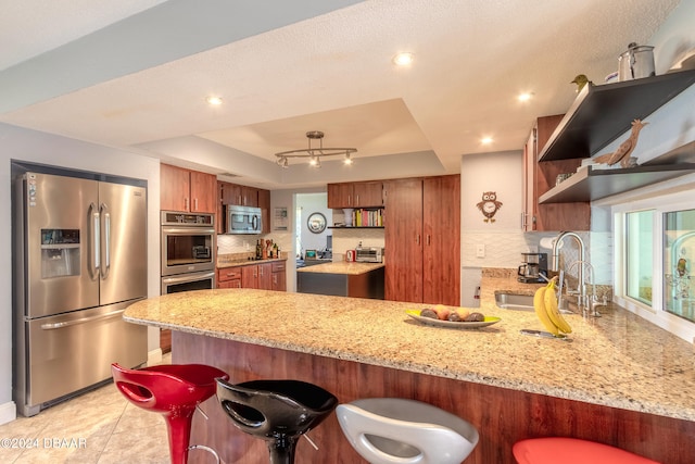 kitchen with stainless steel appliances, kitchen peninsula, decorative backsplash, a kitchen breakfast bar, and a tray ceiling