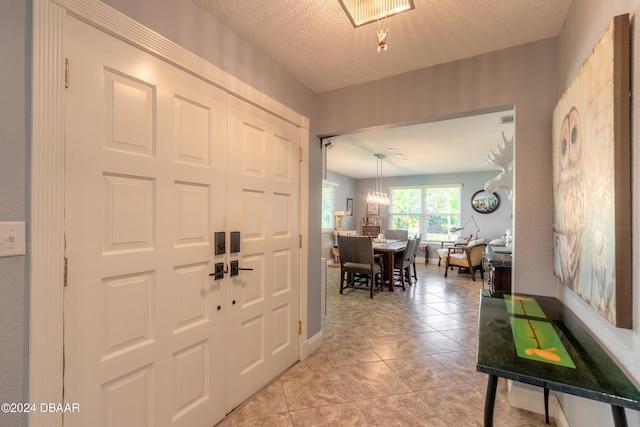 entrance foyer with light tile patterned flooring, a textured ceiling, and an inviting chandelier