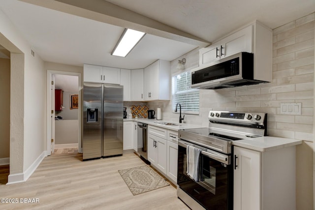 kitchen with sink, white cabinetry, light hardwood / wood-style flooring, appliances with stainless steel finishes, and backsplash