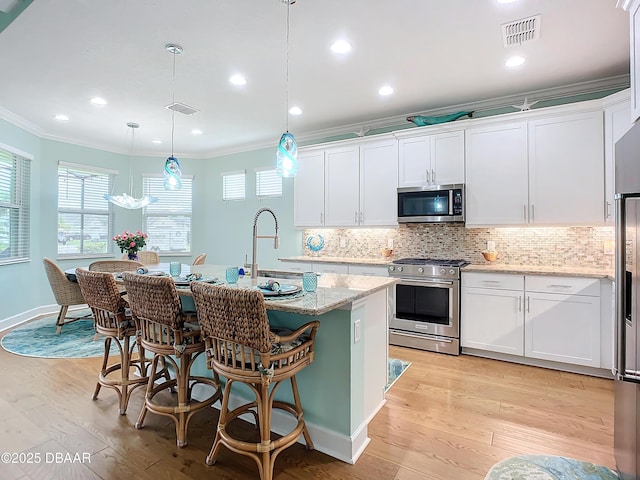 kitchen with a center island with sink, decorative light fixtures, white cabinetry, and stainless steel appliances