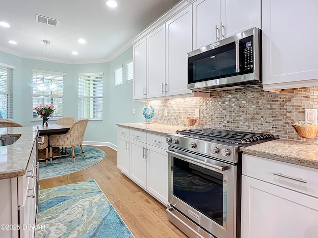 kitchen with light stone countertops, stainless steel appliances, crown molding, decorative backsplash, and white cabinets