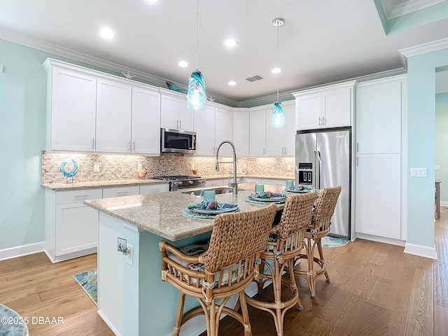 kitchen with light stone countertops, decorative light fixtures, a kitchen island with sink, white cabinets, and high end appliances