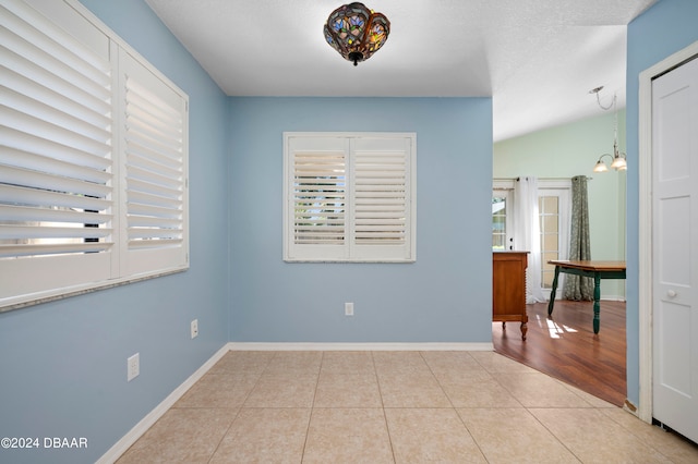 empty room with a textured ceiling, vaulted ceiling, light tile patterned floors, and a notable chandelier