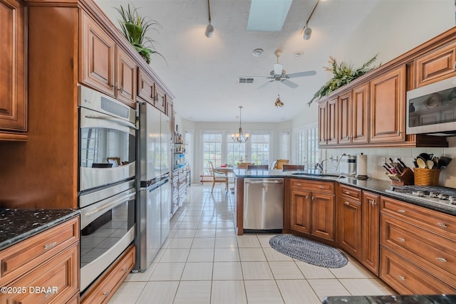 kitchen with sink, light tile patterned floors, ceiling fan with notable chandelier, stainless steel appliances, and decorative light fixtures