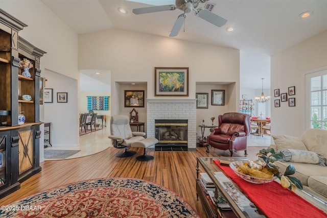 living room featuring lofted ceiling, a brick fireplace, ceiling fan with notable chandelier, and light hardwood / wood-style floors