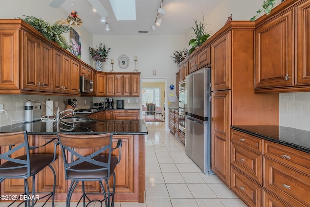 kitchen with a skylight, sink, a breakfast bar area, light tile patterned floors, and stainless steel appliances