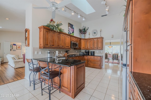 kitchen with light tile patterned floors, appliances with stainless steel finishes, a skylight, a kitchen bar, and dark stone counters