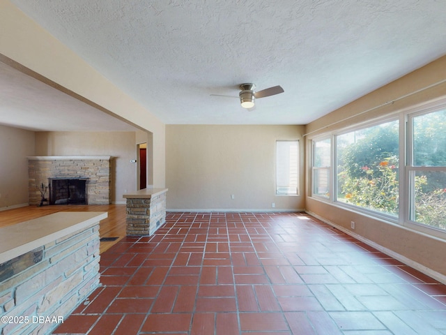 unfurnished living room featuring ceiling fan, a healthy amount of sunlight, a textured ceiling, and a fireplace