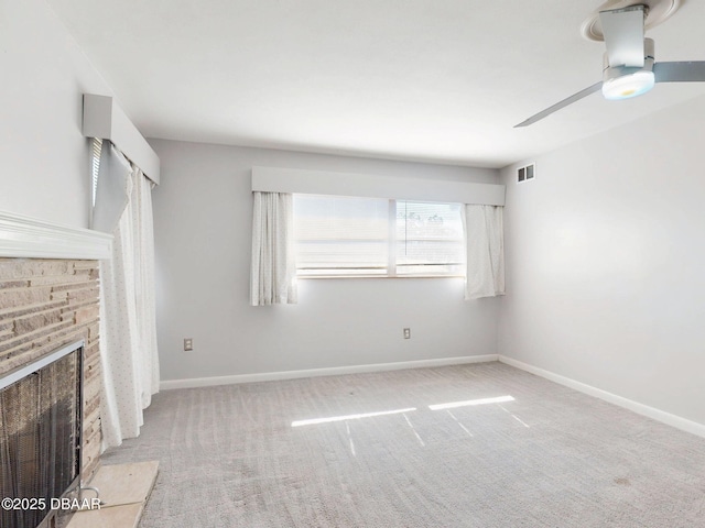 unfurnished living room with ceiling fan, light colored carpet, and a stone fireplace