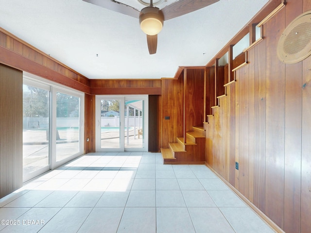 staircase with ceiling fan, tile patterned floors, and wood walls