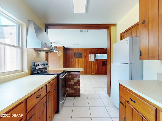 kitchen with stainless steel electric stove, light tile patterned flooring, wooden walls, island exhaust hood, and white fridge