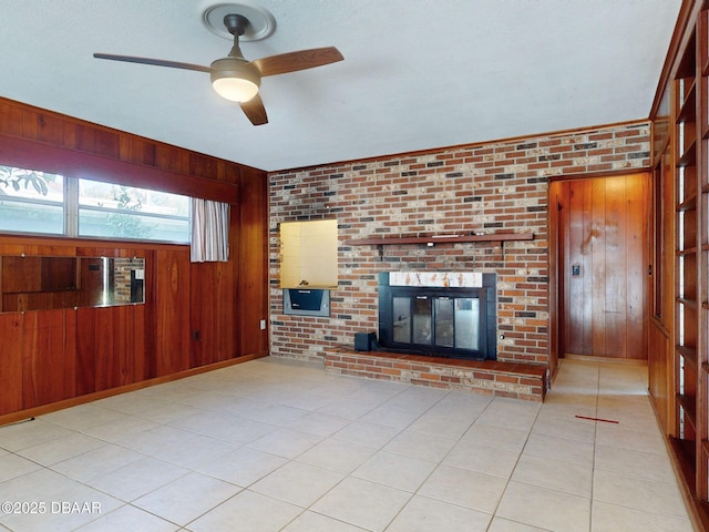 unfurnished living room with light tile patterned flooring, brick wall, wooden walls, ceiling fan, and a brick fireplace