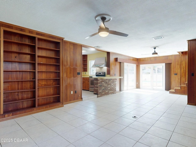 unfurnished living room with a wealth of natural light, wooden walls, built in shelves, and a textured ceiling