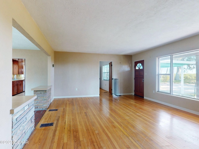 unfurnished living room with a textured ceiling and light hardwood / wood-style flooring