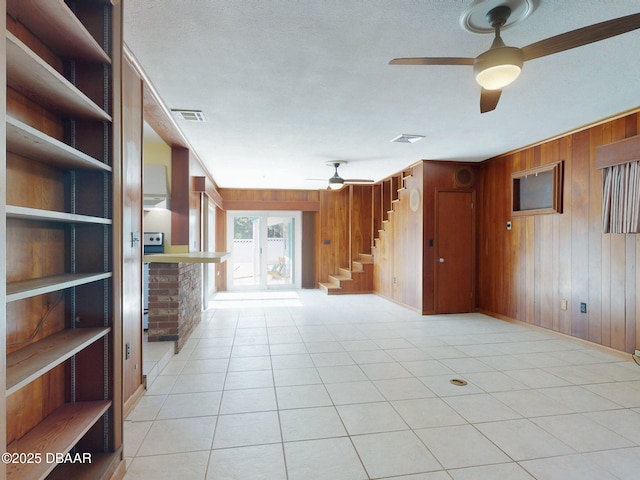 unfurnished living room with light tile patterned floors, a textured ceiling, ceiling fan, and wood walls