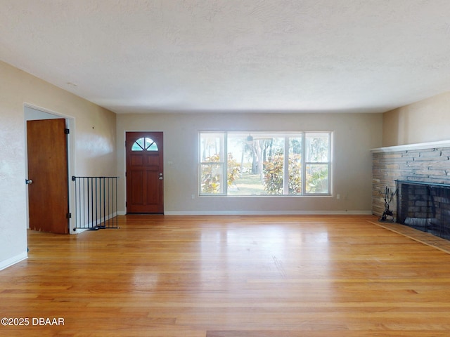 unfurnished living room featuring a stone fireplace, a textured ceiling, and light wood-type flooring