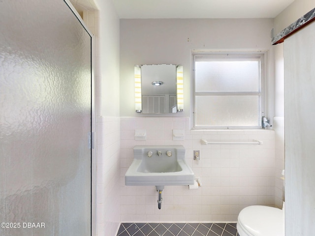 bathroom with toilet, a shower with shower door, sink, and tile walls