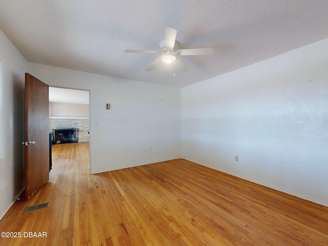 unfurnished room featuring ceiling fan, a fireplace, and light wood-type flooring