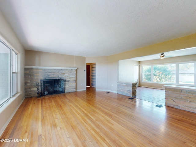 unfurnished living room with a stone fireplace, ceiling fan, and light wood-type flooring