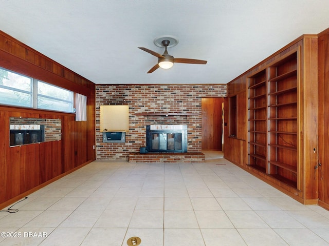 unfurnished living room featuring light tile patterned floors, built in features, ceiling fan, wooden walls, and a fireplace