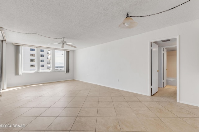 empty room featuring ceiling fan, light tile patterned flooring, and a textured ceiling