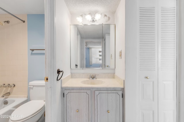 full bathroom with a textured ceiling, vanity, toilet, and tiled shower / bath