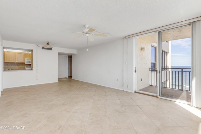 empty room with ceiling fan, light tile patterned floors, a water view, and a textured ceiling