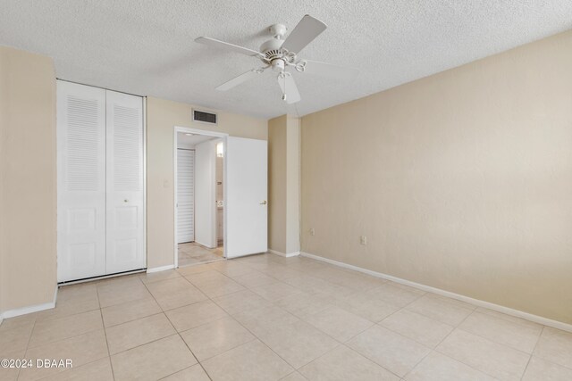 unfurnished bedroom with ceiling fan, a closet, light tile patterned floors, and a textured ceiling