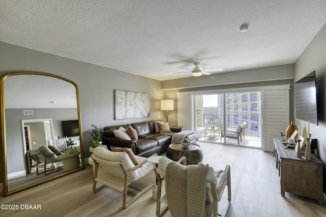 living room with a textured ceiling, light hardwood / wood-style floors, and ceiling fan