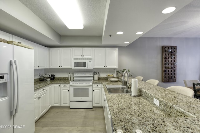 kitchen featuring sink, white appliances, light stone countertops, light hardwood / wood-style floors, and white cabinets