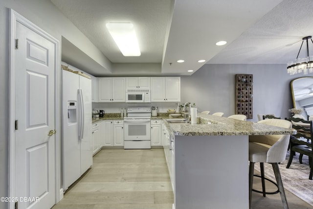 kitchen with pendant lighting, white appliances, a breakfast bar, white cabinets, and light wood-type flooring