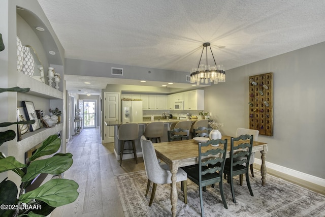 dining space featuring an inviting chandelier, sink, light hardwood / wood-style floors, and a textured ceiling