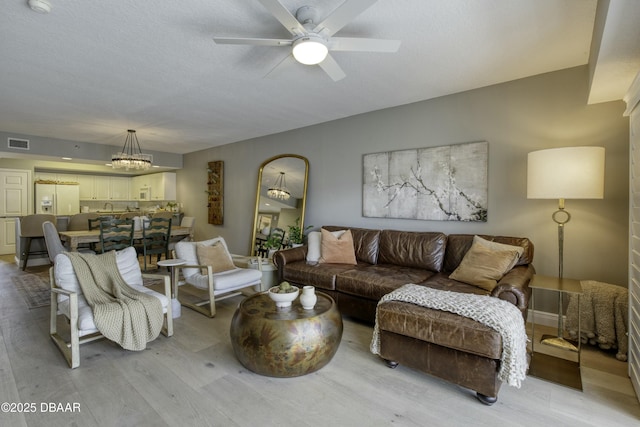 living room featuring ceiling fan with notable chandelier, a textured ceiling, and light wood-type flooring