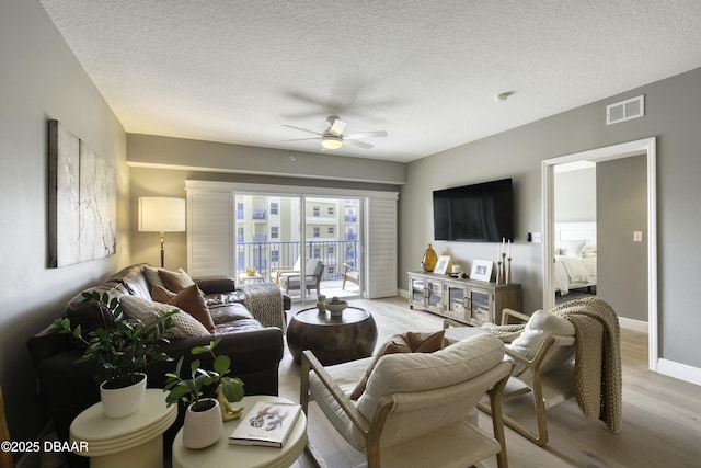 living room featuring ceiling fan, light hardwood / wood-style flooring, and a textured ceiling