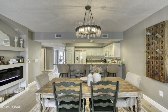 dining room featuring built in shelves, sink, a textured ceiling, light hardwood / wood-style flooring, and a notable chandelier