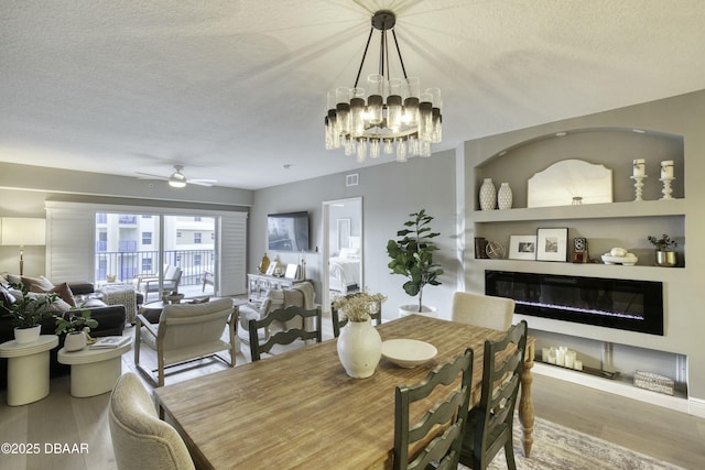 dining room with ceiling fan with notable chandelier, hardwood / wood-style floors, a textured ceiling, and built in shelves