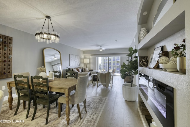 dining room with wood-type flooring, ceiling fan with notable chandelier, and a textured ceiling