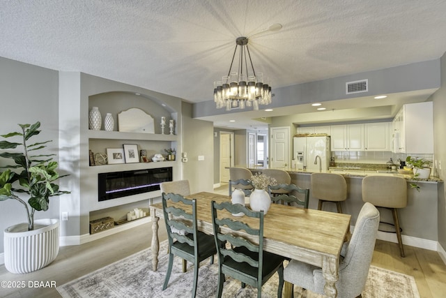 dining space with an inviting chandelier, built in features, light hardwood / wood-style floors, and a textured ceiling