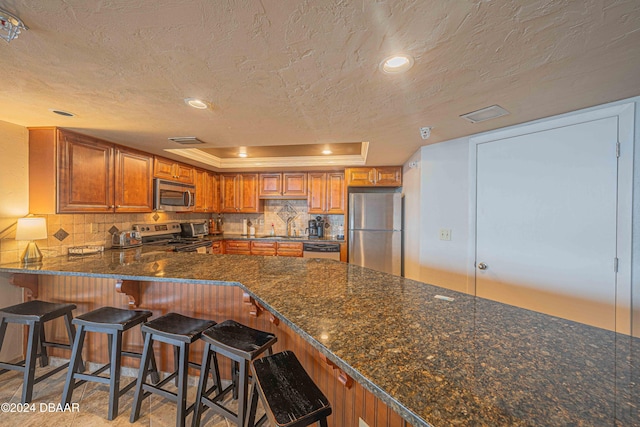 kitchen featuring stainless steel appliances, a textured ceiling, kitchen peninsula, and tasteful backsplash