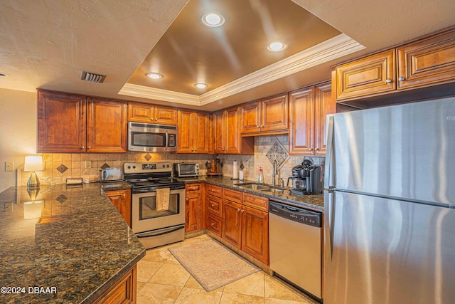 kitchen with stainless steel appliances, dark stone counters, decorative backsplash, and a tray ceiling